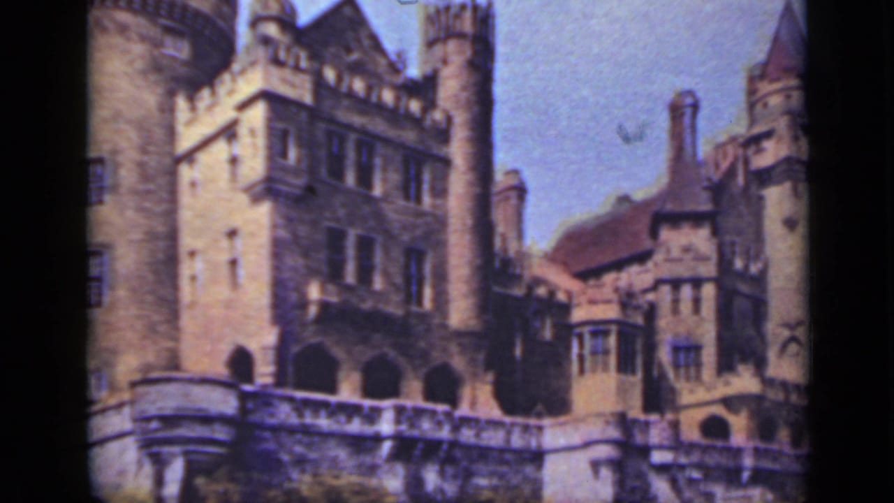 Stone castle facade with towers, arched openings, and blue sky.