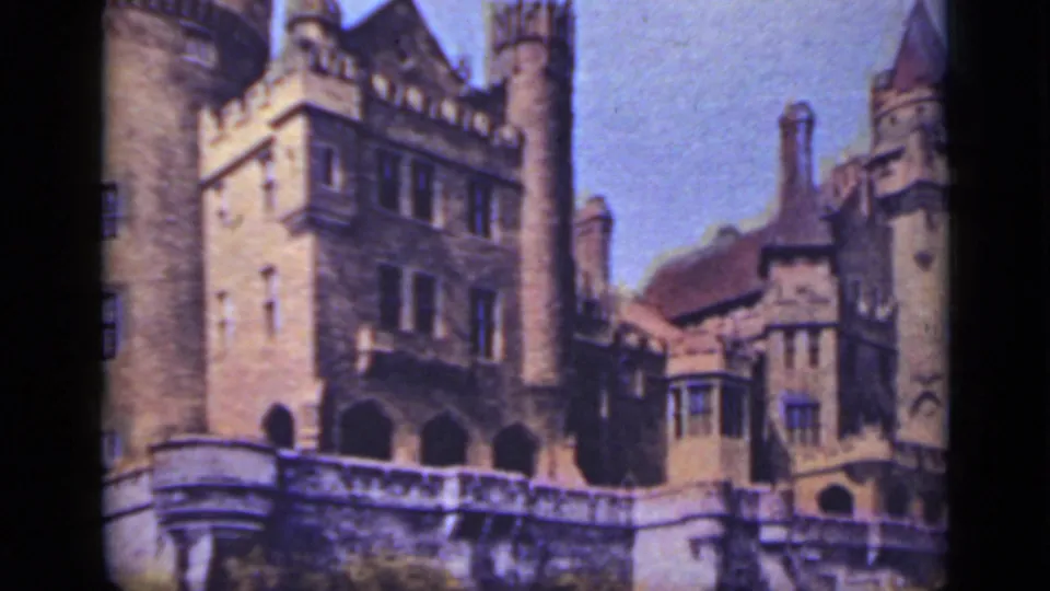 1940 Ontario 8mm frame of a stone castle-like building with turrets, windows, and a bird crossing the blue sky.