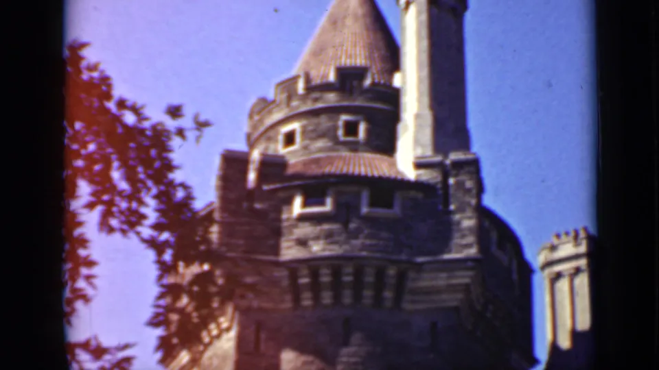 1940 Ontario 8mm frame showing a round stone turret, steep roof, chimney, and tree branches against blue sky.
