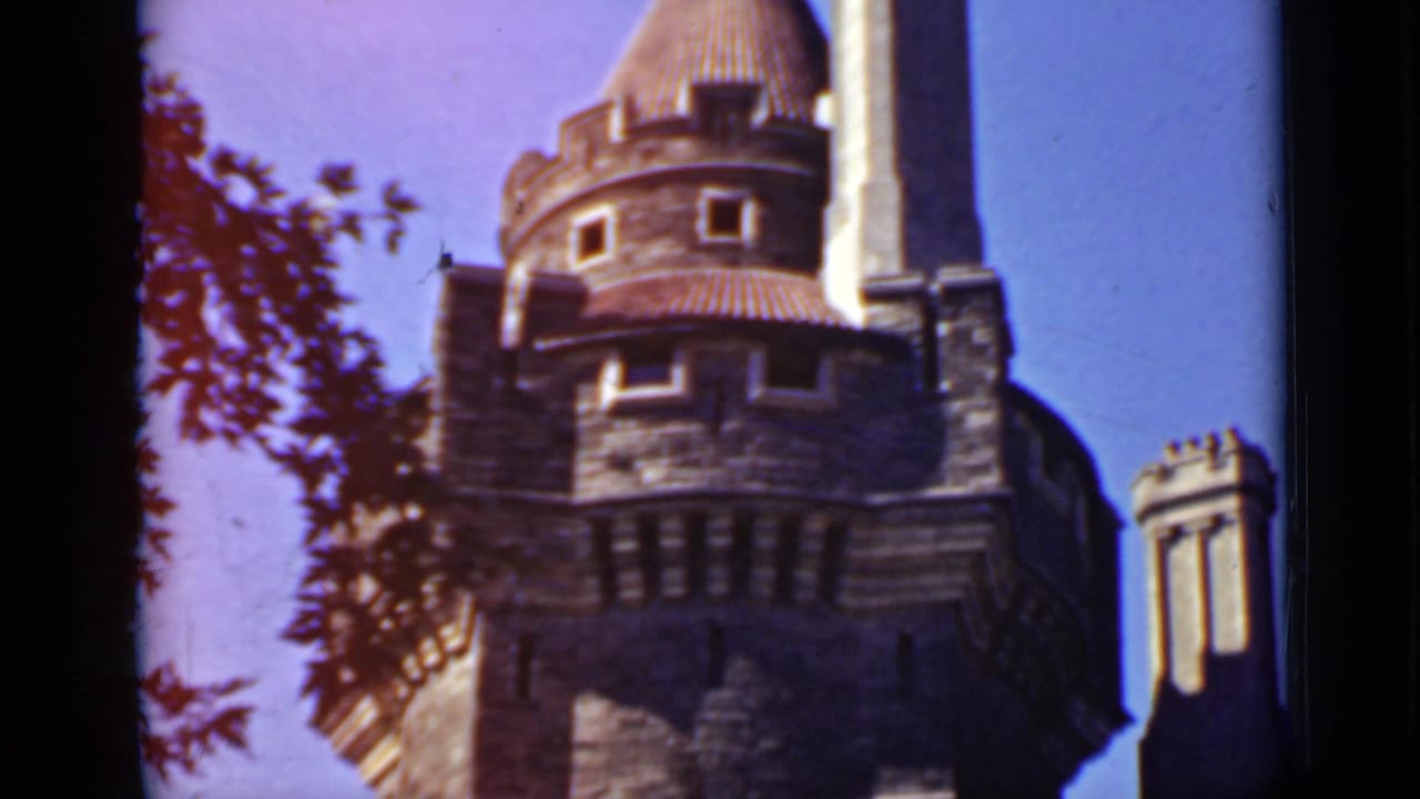 Low-angle 1940 Ontario home-movie view of a stone tower under blue sky, framed by dark film edges and nearby branches.