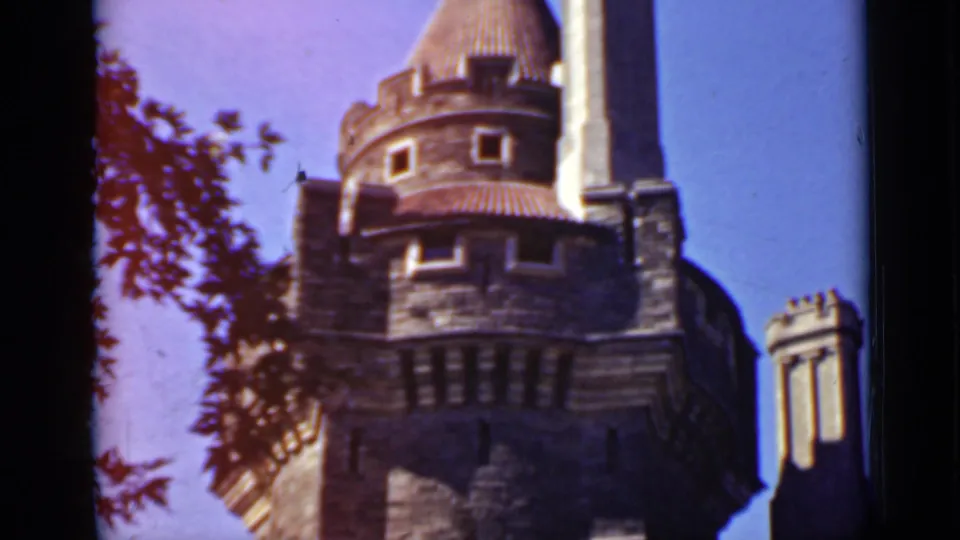 Low-angle 1940 Ontario home-movie view of a stone tower under blue sky, framed by dark film edges and nearby branches.