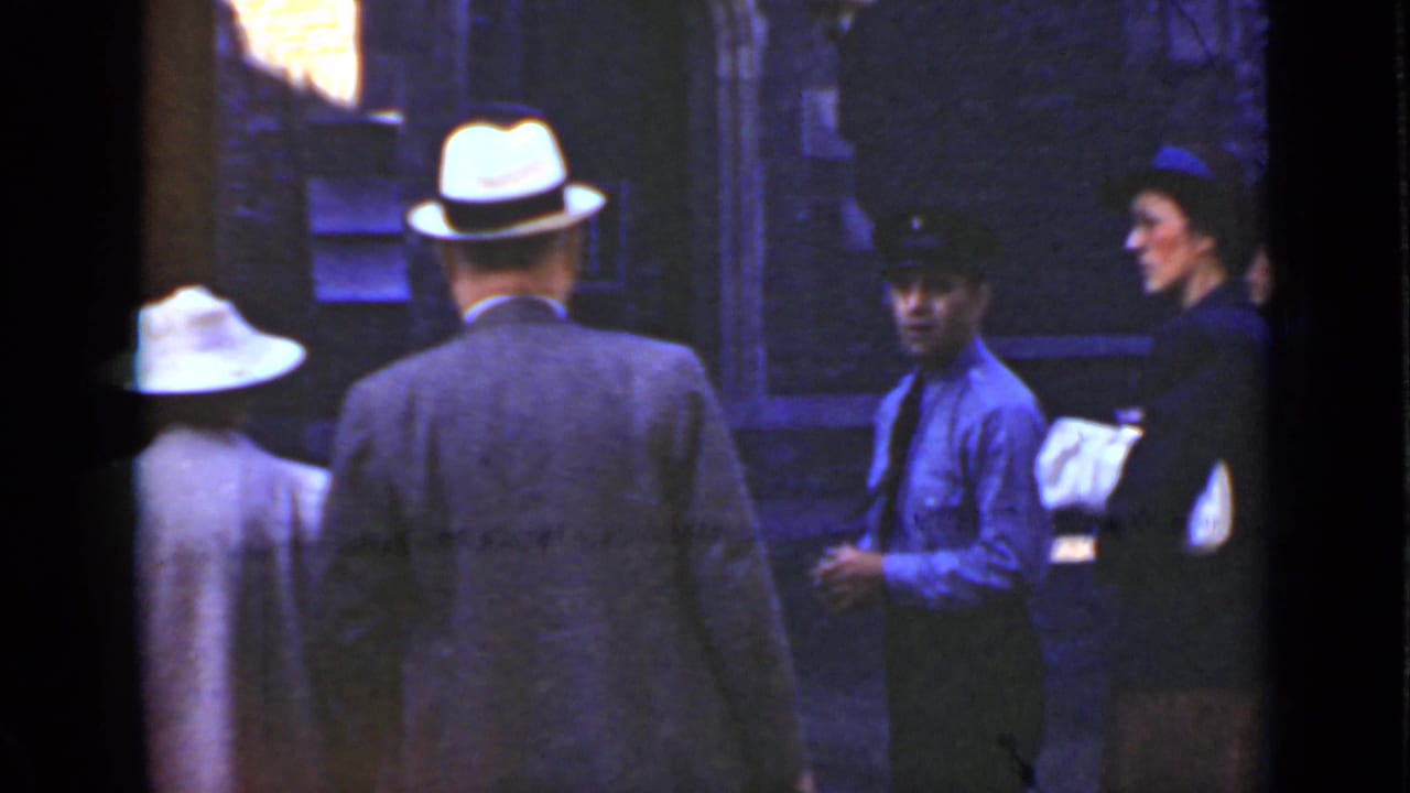 Several adults in hats stand on a dock near a uniformed worker and waterfront structures.