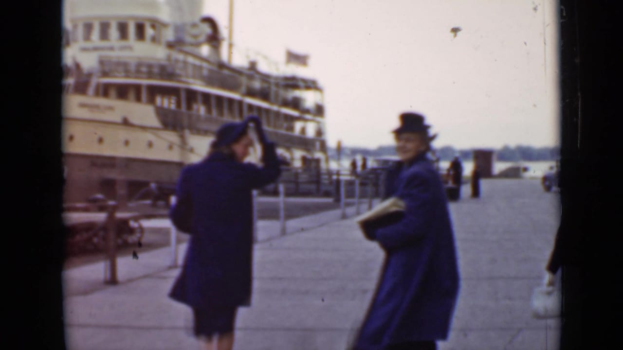 Two women on a dock near a large passenger ship, one facing the camera.
