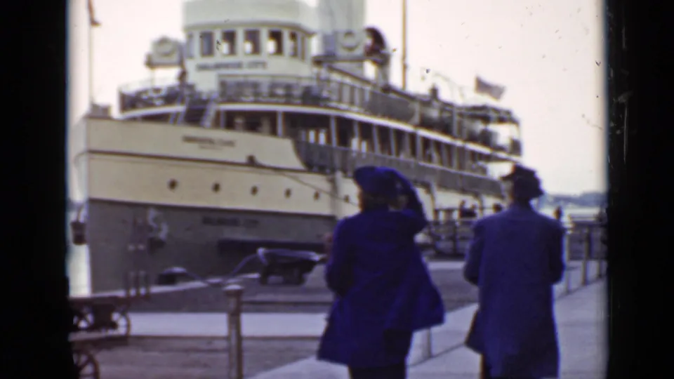 Two women in dark coats walk along an Ontario dock beside a multi-deck passenger ship in this 1940 home-movie frame.
