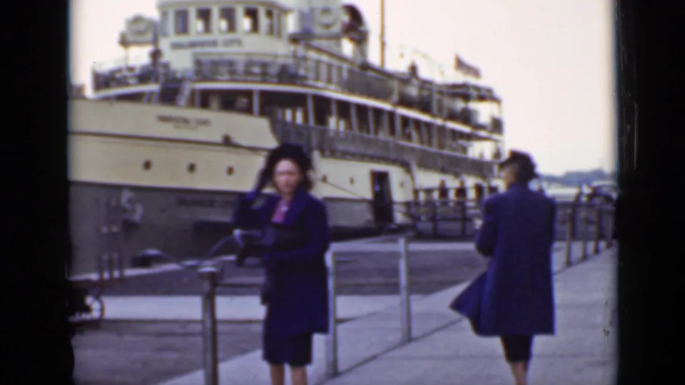 On the dock in Ontario, one woman turns toward the camera while another remains near the railings and passenger ship.