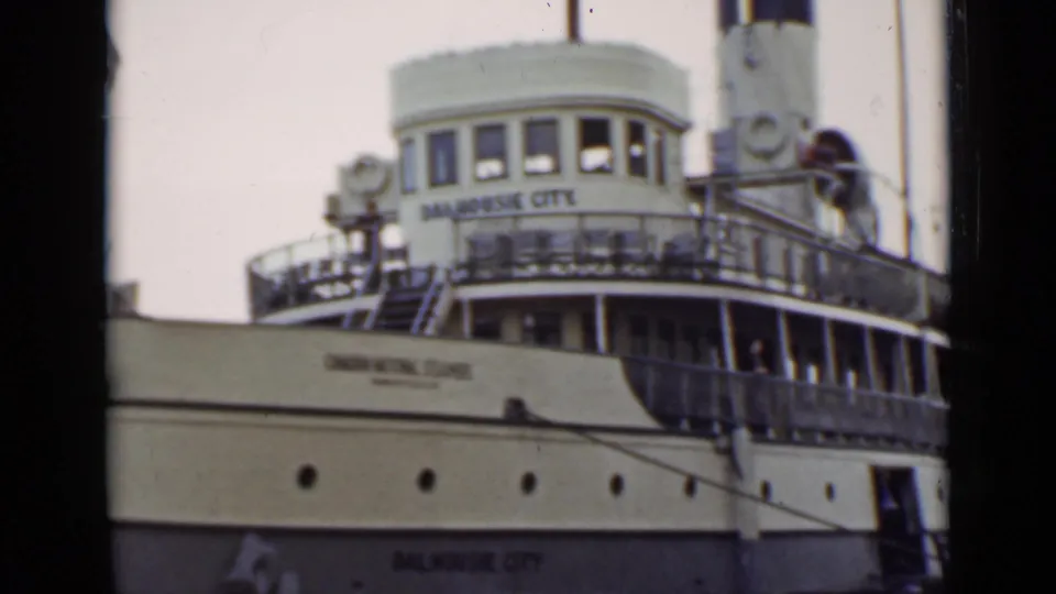 The Dalhousie City appears at an Ontario dock, with its white wheelhouse, railings, and cream hull seen in soft 8mm color.