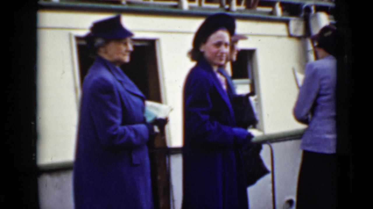 Women in coats and hats wait beside a boat or dock railing.