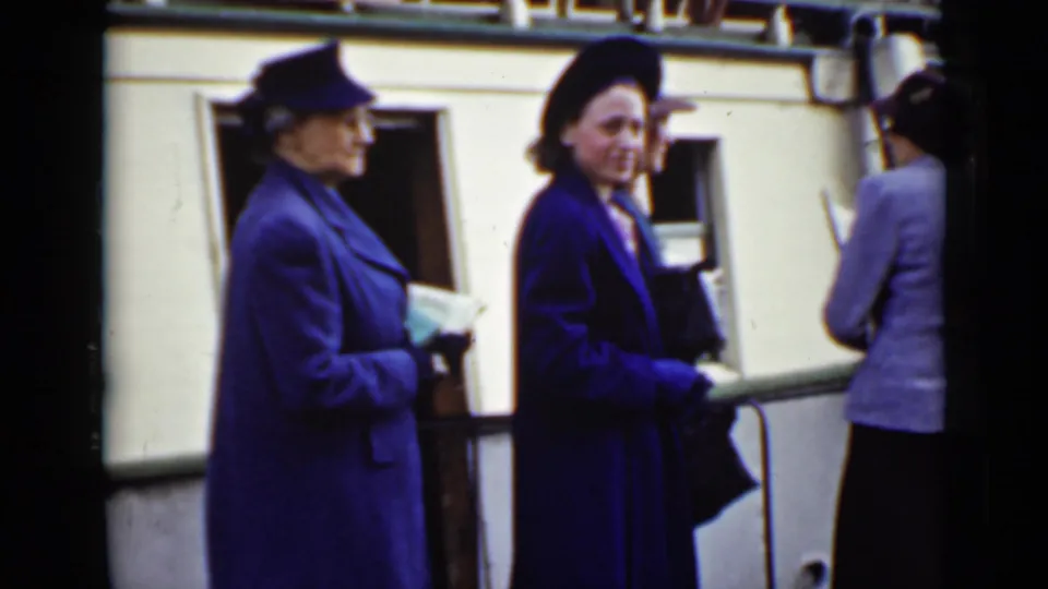 In 1940s Ontario home-movie footage, women in dark coats and hats stand near a boat or dock structure, one holding papers.