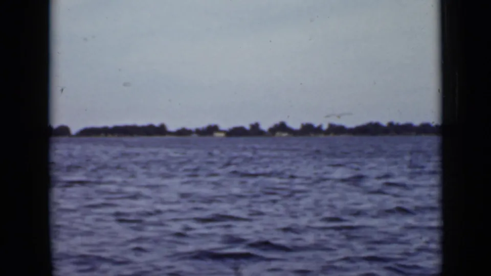 1940 Ontario 8mm frame showing open water, a low wooded shoreline, pale sky, and visible film gate edges.