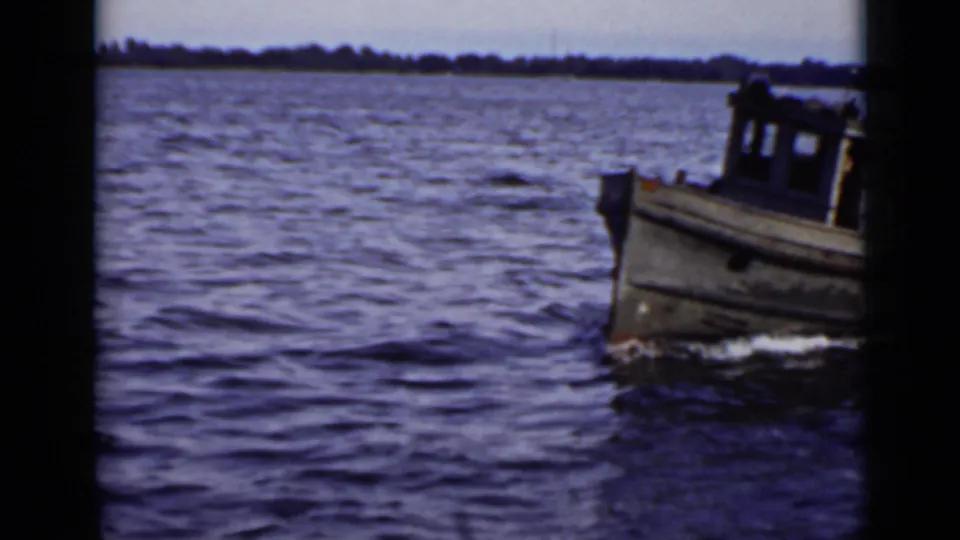 Small cabin boat moves across rippling Ontario water, with shoreline in the distance and 8mm film borders visible.