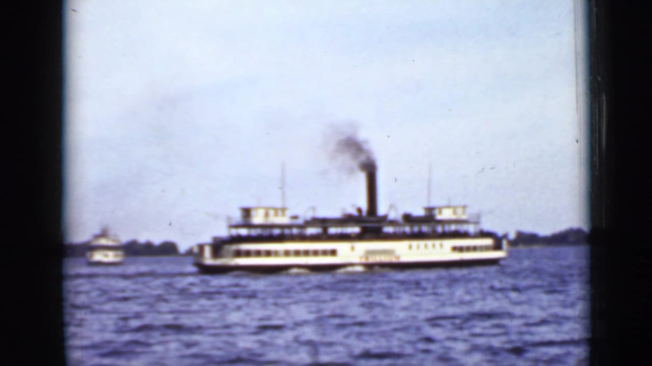 Steam ferry crossing wavy water with smoke rising from its stack.