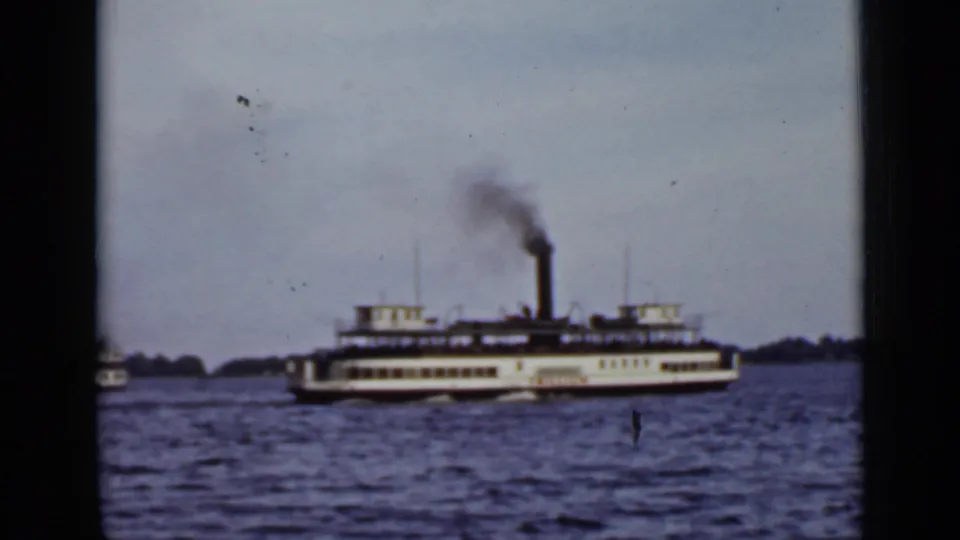 The ferry continues across Ontario lake water, with its tall stack emitting smoke and the image softened by 8mm grain.