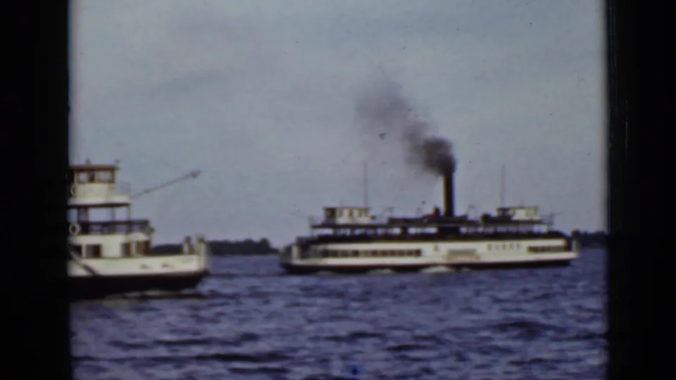 A small motorboat passes near the camera while the steam ferry continues behind it on Ontario lake waters.