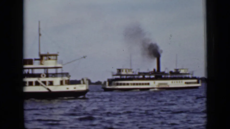 1940 Ontario 8mm frame showing two white ferries on a lake, one emitting dark smoke from a tall stack.