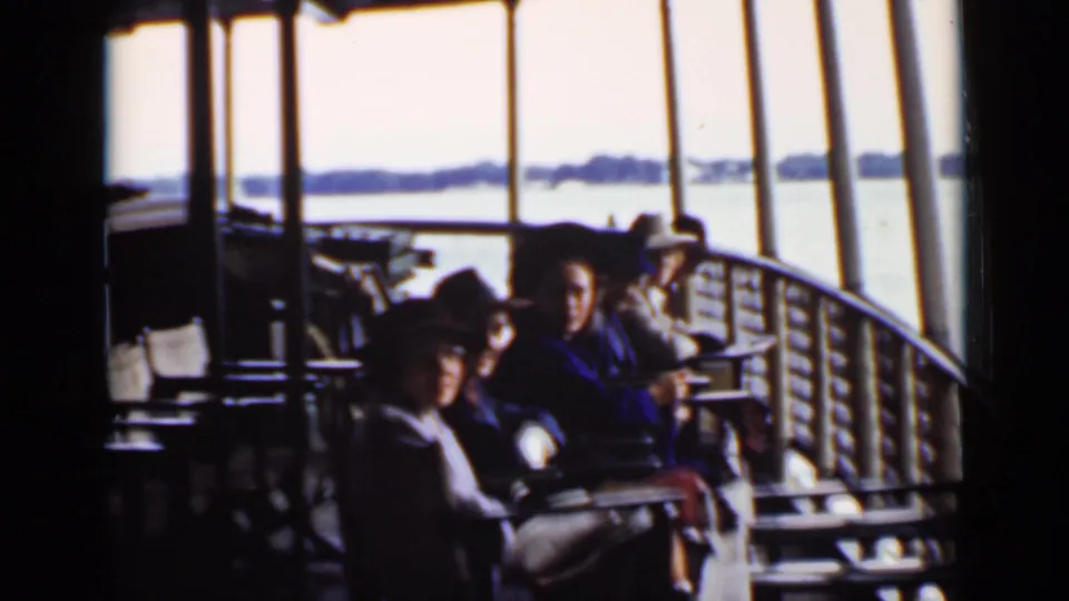 In 1940 Ontario home-movie footage, passengers sit on a covered ship deck with railings, posts, and water in the background.