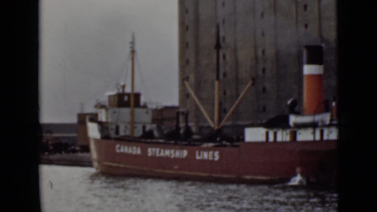 1940s Ontario harbor view of a red Canada Steamship Lines vessel moored near a tall grain elevator.