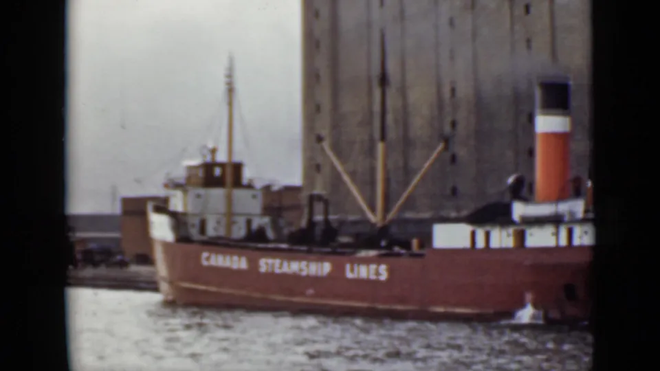 Red-hulled Canada Steamship Lines vessel in an Ontario port, framed against a massive grain elevator.
