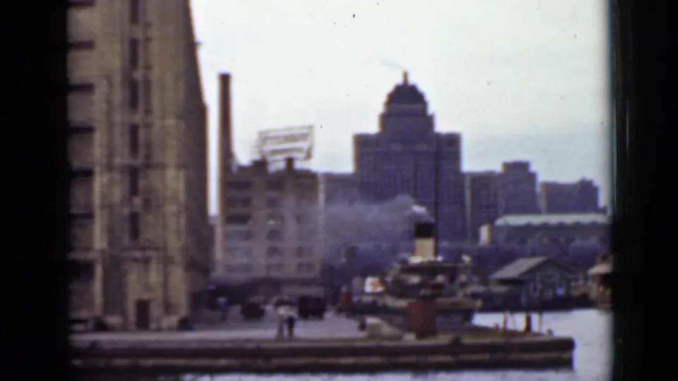 1940s Ontario waterfront looking toward industrial buildings, a distant domed structure, dock activity, and harbor water.