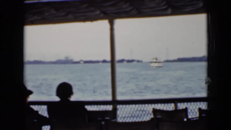 Passengers in silhouette sit inside a ferry on an Ontario harbor crossing, with open water, distant boats, and shoreline beyond the window.