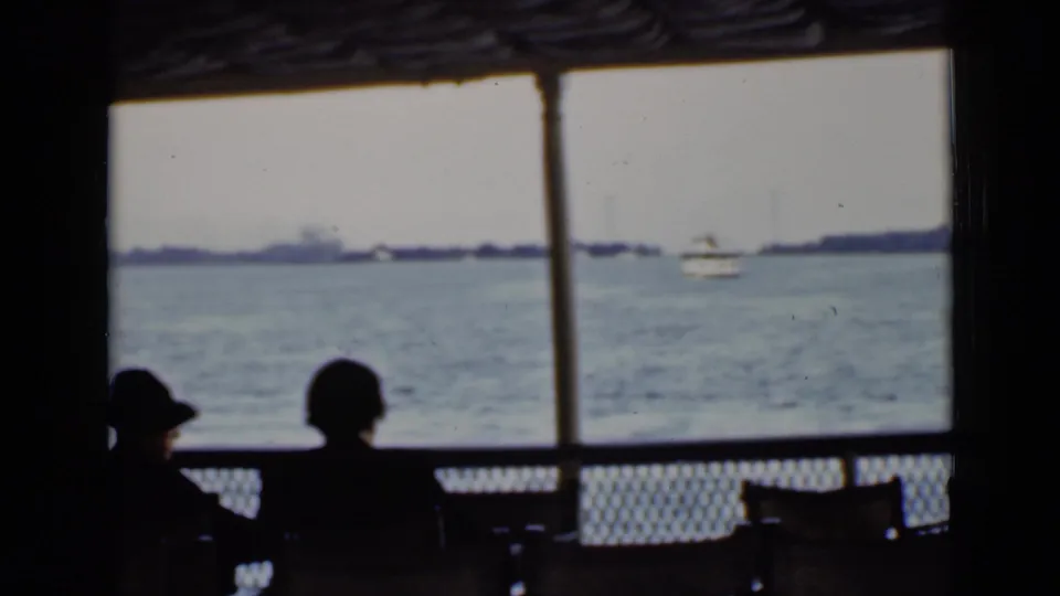 Inside the ferry, two passengers appear in silhouette against an Ontario harbor view with open water, distant shoreline, and a small boat.