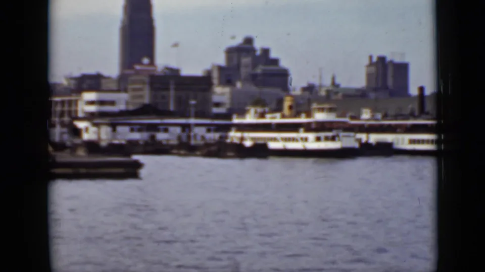 1940 Ontario harbor view with passenger vessels near docks and an urban skyline seen through dark film-frame edges.