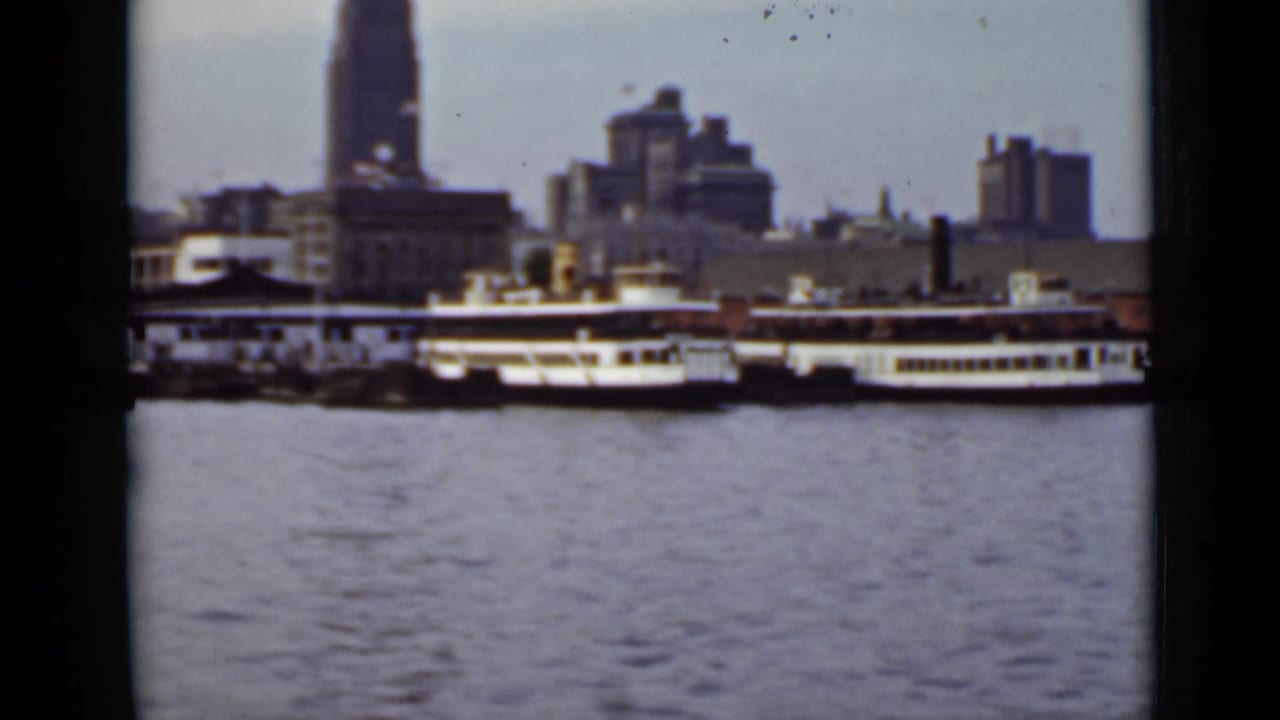Passenger ferries on water with a distant city skyline behind them.