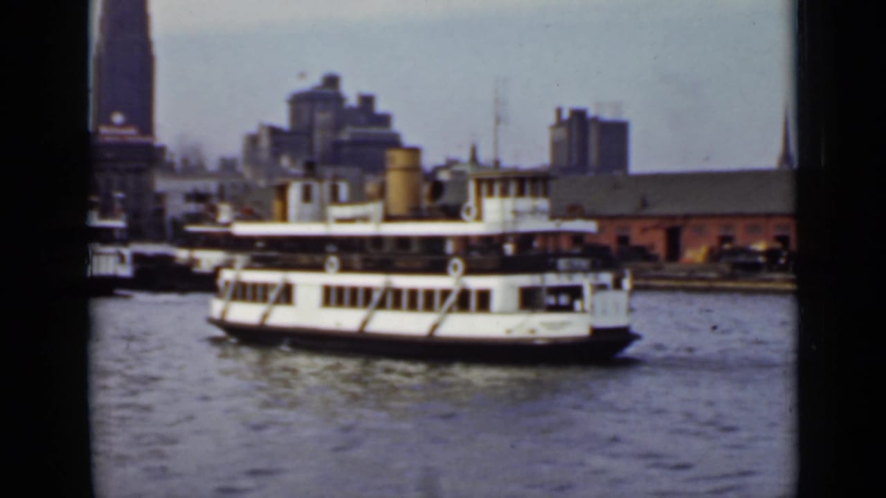 White ferry crossing harbor water with waterfront buildings in the background.