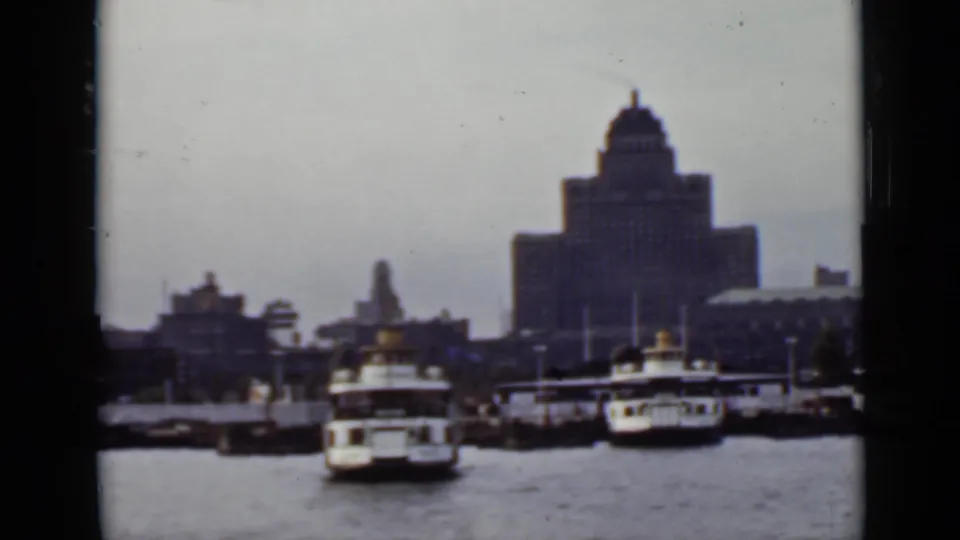 1940s Ontario harbor frame with several ferries by the docks and a large domed building beyond the water.