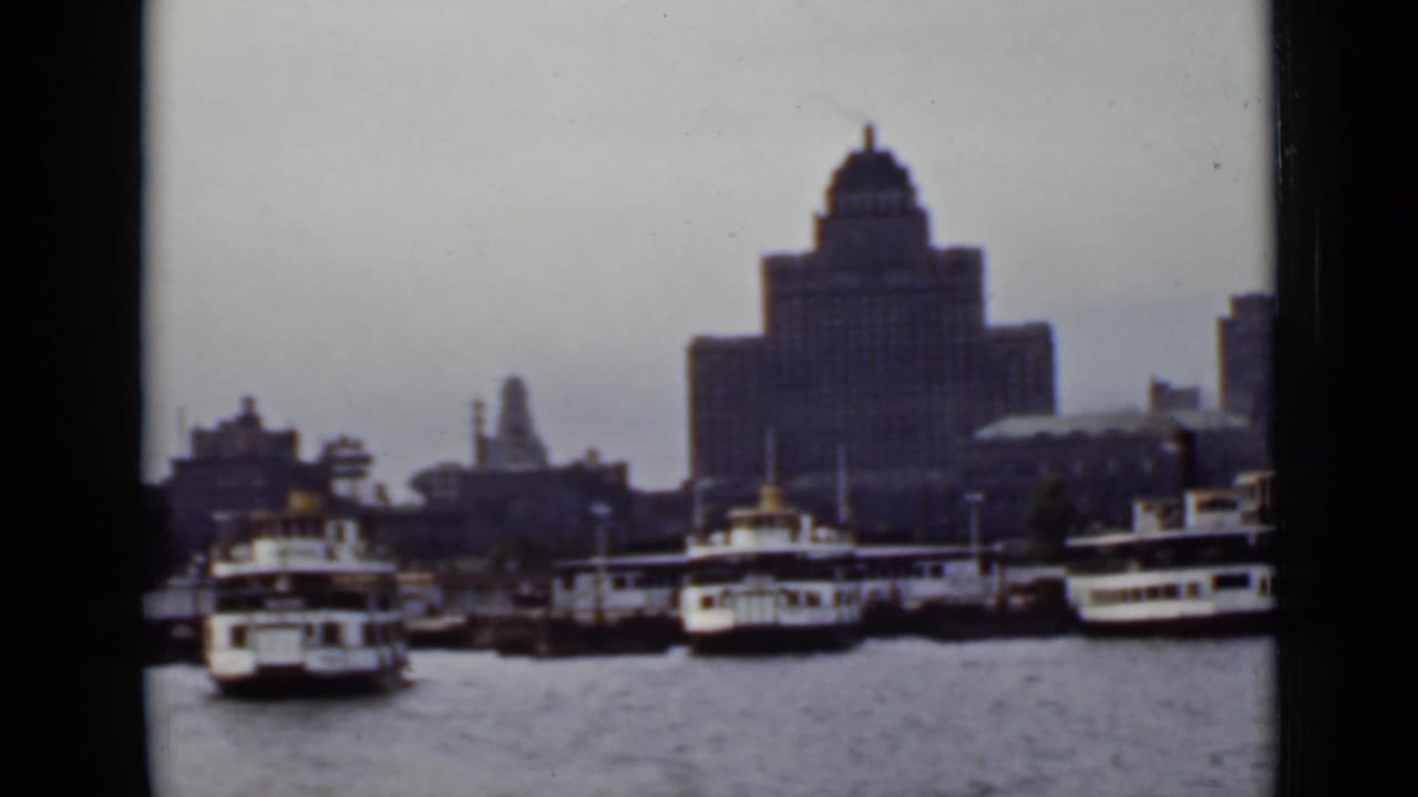 Passenger boats docked along a waterfront with a large towered building behind them.