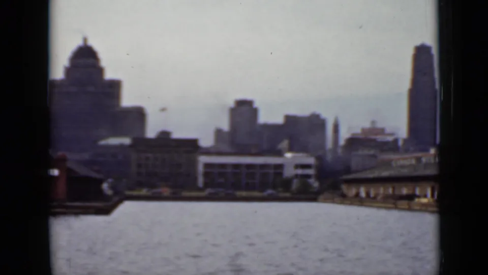 1940 Ontario waterfront frame showing a domed building, distant towers, open water, and the edge of the steamship wharf.