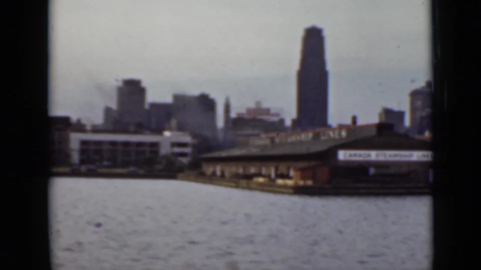 1940 Ontario waterfront view from a boat, with a tall skyscraper, river foreground, and Canada Steamship Lines terminal area.