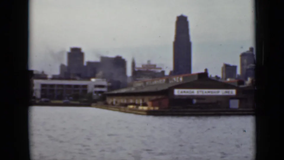1940 Ontario skyline seen from the water, with a prominent tower and waterfront terminal structures in soft 8mm color.