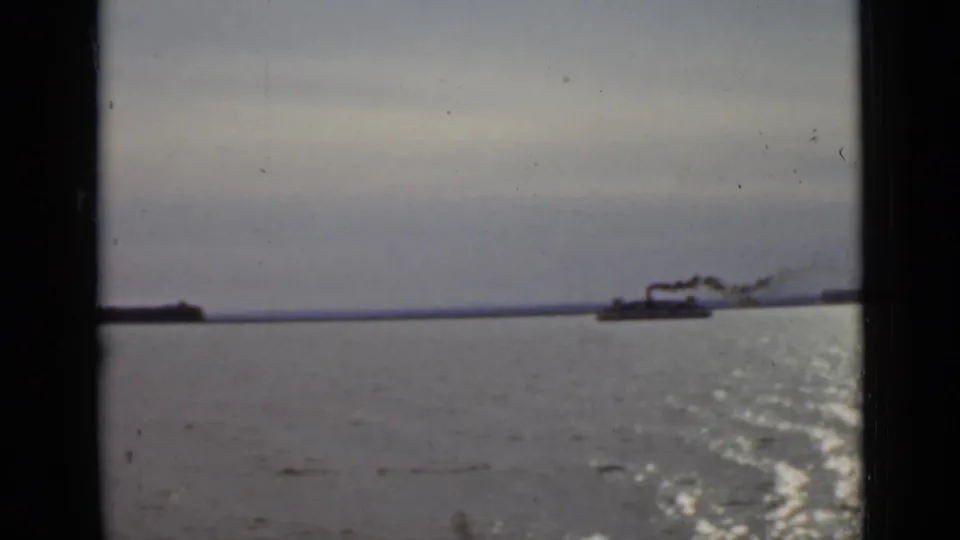 1940 Ontario river scene from a moving boat, showing a distant smokestack vessel and bright reflections on the water.