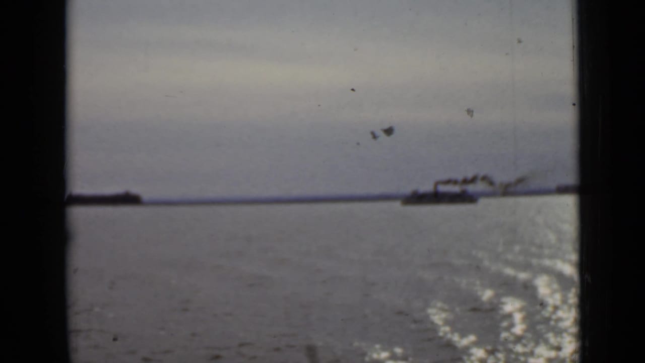 Distant smoking vessel crossing open water under a muted sky.