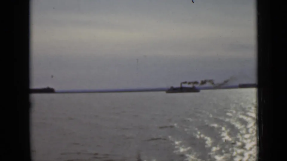 A distant smoking boat appears on the Ontario waterfront, with bright wake patterns and dark frame edges from the 8mm scan.