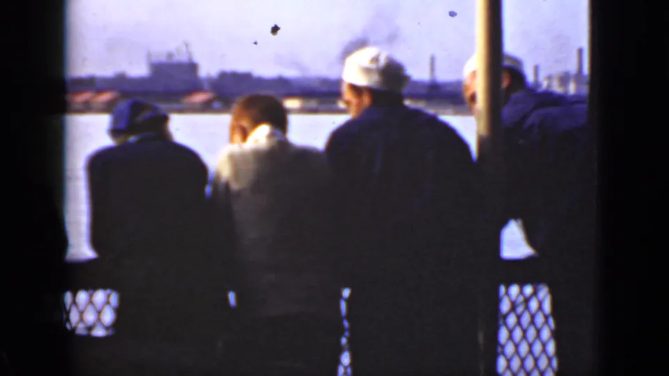 1940 Ontario home-movie frame showing uniformed men at a boat rail, with water, buildings, and smokestacks in the background.