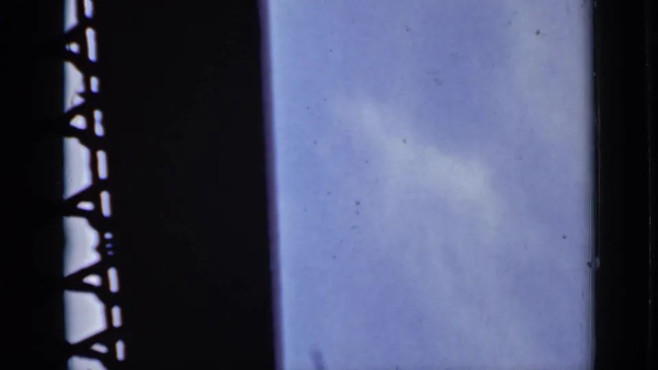 A pale blue sky and dark bridge support dominate the final frame, with visible dust and fading from the 8mm scan.