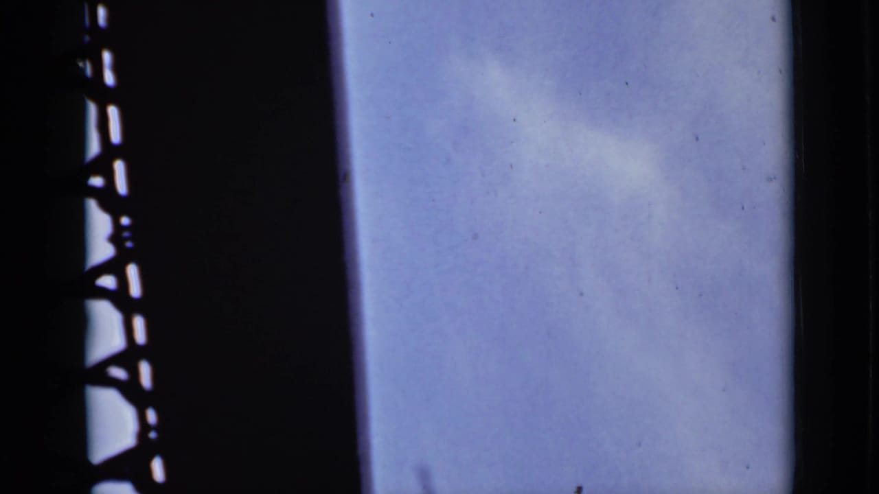 Pale blue sky and thin cloud seen beside a dark silhouetted metal structure.