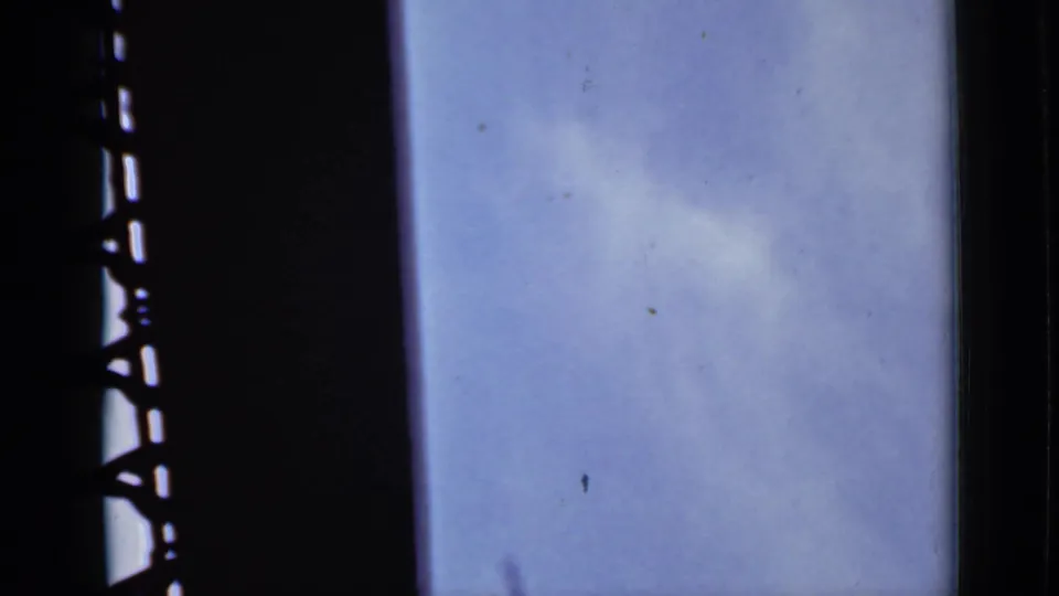1940 Ontario 8mm frame with wispy cloud, blue sky, and a dark silhouetted structural edge crossing the left side.