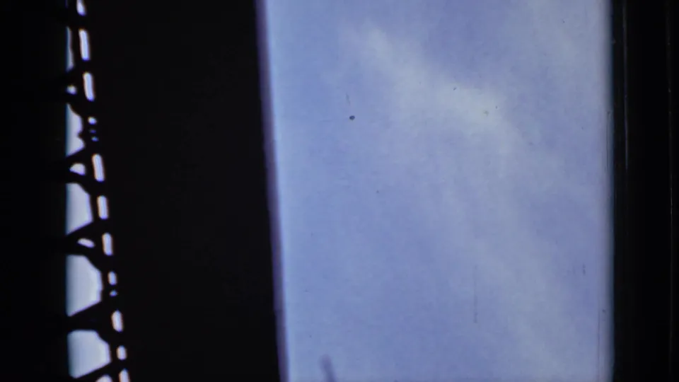1940 Ontario 8mm frame showing soft cloud patches and blue sky partially blocked by a dark metal or window-side silhouette.