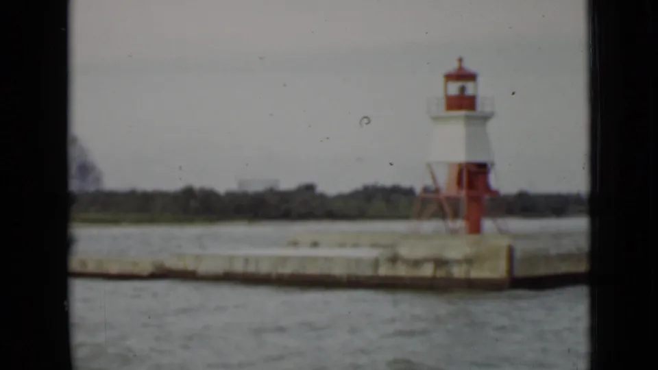 1940 Ontario boat-view frame showing a red-and-white pier light centered on a concrete harbor structure with water in the foreground.