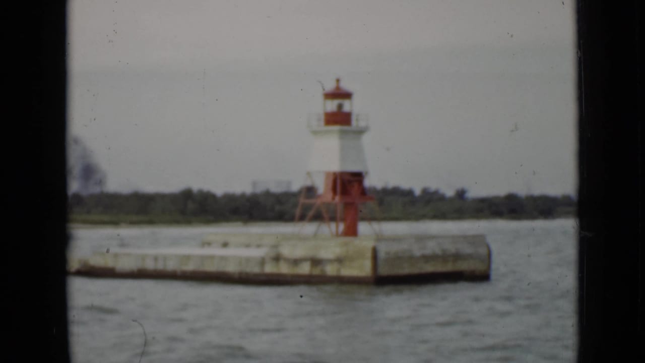 Small red and white lighthouse on a concrete pier beside choppy water.