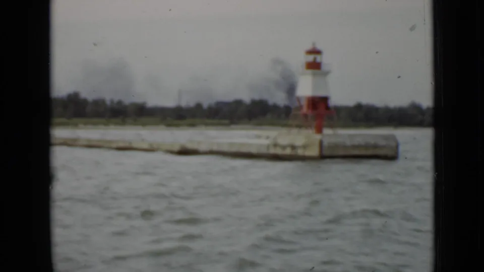 1940 Ontario harbor approach showing the lighthouse shifted right in frame, with choppy water and trees behind the pier.