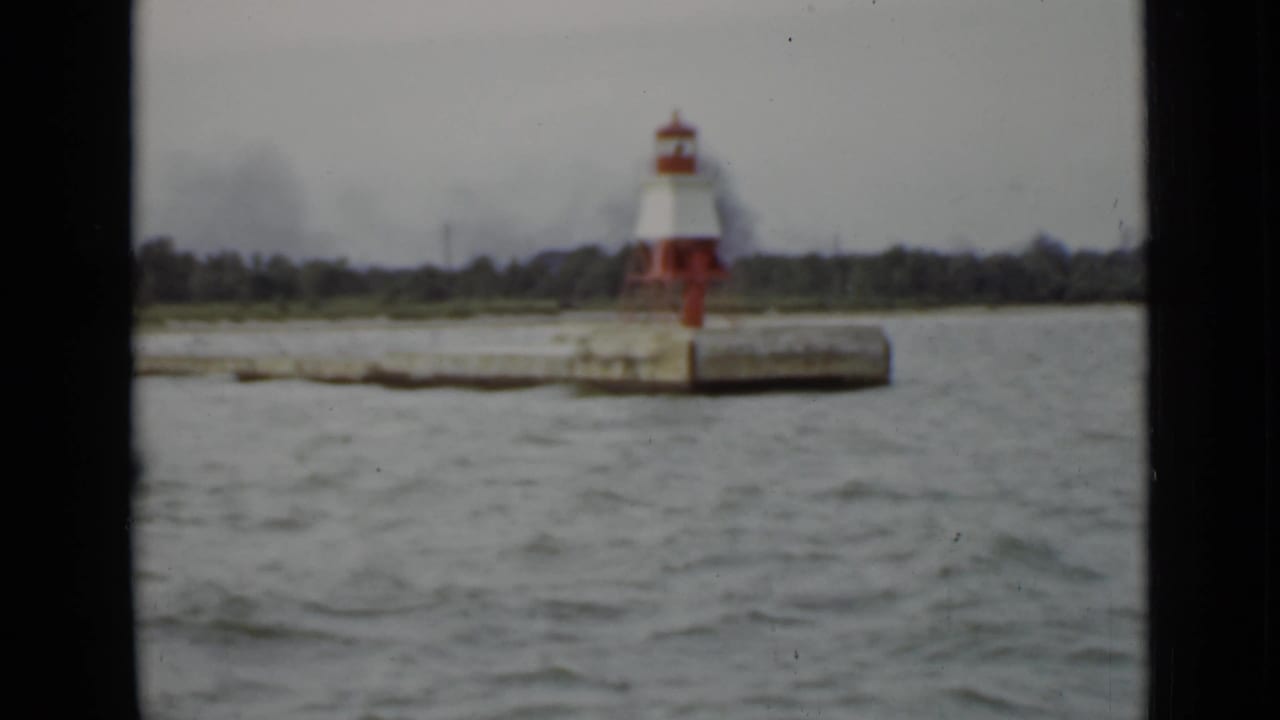 Red-and-white lighthouse on a concrete pier seen across gray water under an overcast sky.