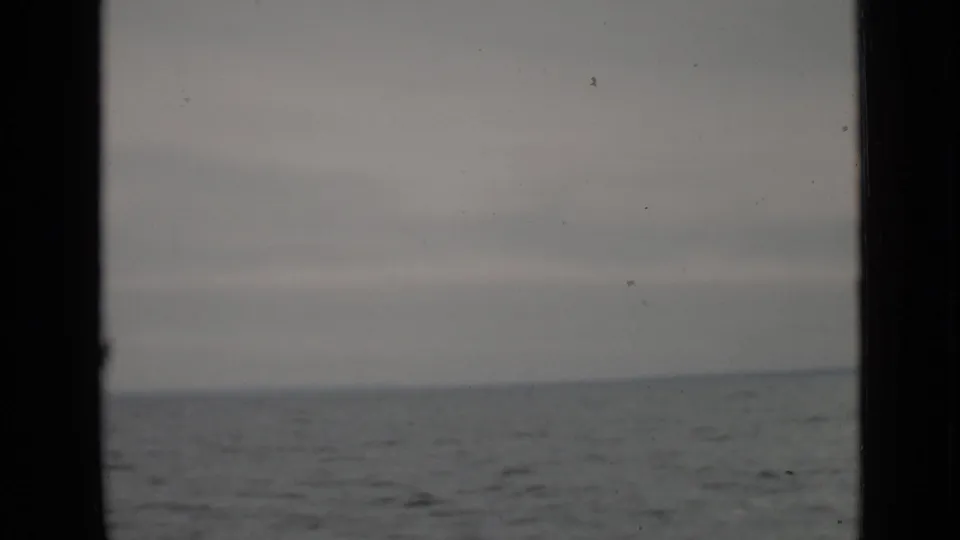 1940 Ontario 8mm frame showing the boat's view across gray lake water, with an overcast sky and visible film gate framing.