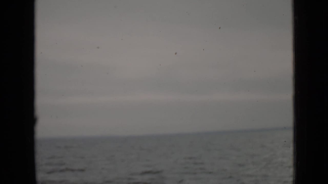 Gray lake water seen through a dark window or doorway under an overcast sky.