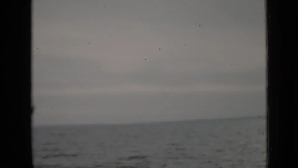 1940 Ontario home-movie frame showing a gray lake horizon through a dark vertical window or doorway edge, with muted sky and water.