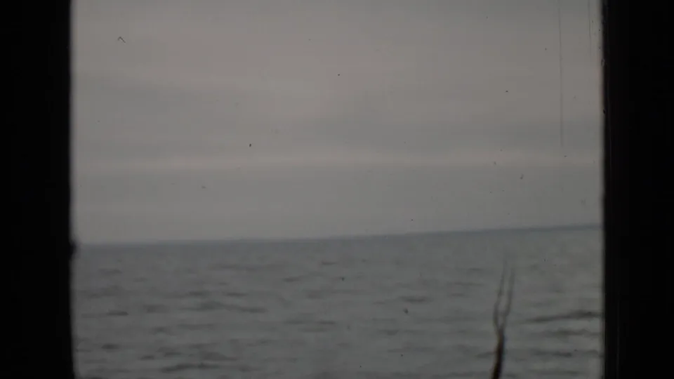 1940 Ontario home-movie view of rippled gray lake water under a cloudy sky, with dark framing at the side and a thin foreground branch.