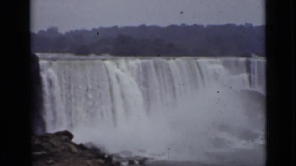 1940 8mm view of American Falls with a dark rock edge in the foreground and a broad curtain of water dropping into mist.
