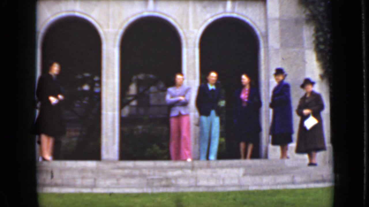 Six adults stand on steps before a stone building with arched entrances.